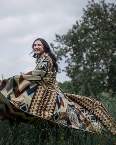 a woman is sitting in the grass with a blanket on her back and smiling at the camera