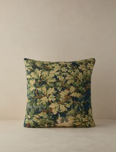 a green and blue pillow with leaves on it, sitting on a white table next to a wall