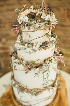 a three tiered wedding cake with flowers and greenery on the top is sitting on a table