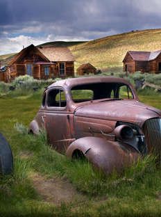 an old rusted car sits in the middle of a grassy field next to some cabins