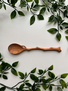 a wooden spoon sitting on top of a table next to some green leafy branches