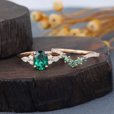 an emerald and diamond ring sitting on top of a piece of wood