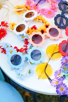 colorful sunglasses are sitting on a table with flowers around them and one is wearing sun glasses