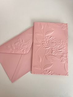 two pink envelopes sitting on top of each other next to an envelope with flowers