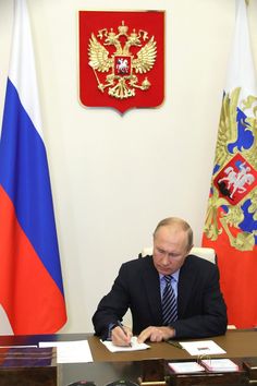 a man sitting at a desk with papers in front of him and two flags behind him