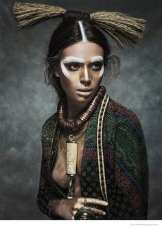 a woman with white paint on her face holding a camera and wearing a headdress