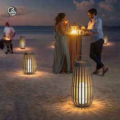 two people standing next to each other on a beach at night with lights in the sand