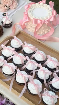 cupcakes are arranged on a wooden tray with pink ribbons and flowers in the background