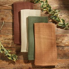 three different colored towels sitting on top of a wooden table next to leaves and ivy