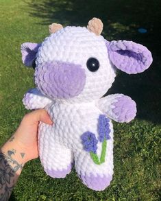 a hand holding a crocheted purple and white cow with flowers on it's chest