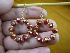 a pair of red and gold beaded earrings sitting on top of a wooden stick