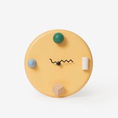 a yellow clock with two different colored balls on it's face and one green ball in the middle