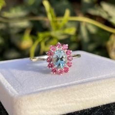 a blue ring with pink and white stones sits on top of a cloth covered box