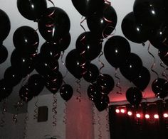 many black balloons are hanging from the ceiling in a room with red lights and curtains