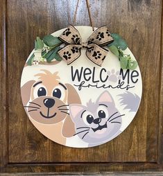 a wooden door with a welcome sign and two cats hanging from it's side