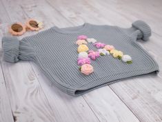 a knitted sweater with flowers on it laying on the floor next to some sunglasses