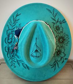 This teal, hand burned fedora, features a flower motif. Made from premium faux suede with cotton and leather banding. She has all the western elements making her wild and bold! I use only the best materials for my hats and each one is handcrafted and uniquely one of a kind.  This hat has an adjuster inside the crown that allows 22-22.9 inch circumference; she fits most sizes. Brim length - 3.75" Height - 4.72" Due to the nature of my hats and because of various sanitary concerns, hats are NOT re Handmade Brimmed Fedora For Ranch, Handmade Western Fedora For Western-themed Events, Artisan Fedora With Short Brim For Rodeo, Handmade Western Fedora For Country Events, Custom Handmade Fedora For Country Events, Handmade Country Style Fedora For Western-themed Events, Artisan Short Brim Fedora For Rodeo, Handmade Hats For Rodeo, Handmade Wide Brim Fedora For Ranch