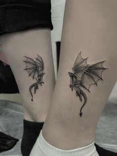 two small tattoos on the legs of people with dragon wings and flowers tattooed on them