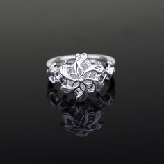 a silver ring with an intricate design on the front and center, sitting on a black surface