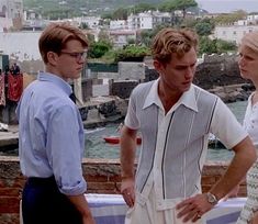 two men and a woman standing next to each other in front of a body of water