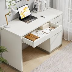 a laptop computer sitting on top of a white desk next to a potted plant