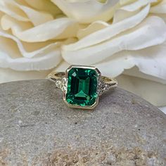 "The ring pictured is lab created emerald with moissanite accents #6974 -Approximate total carat weight: approx. 3.67ctw diamond equivalent -Center Stone Size: 10x8mm - approx. 3.55ct diamond equivalent -Center Stone Shape: emerald cut -Gem Type: lab created emerald -Stone Clarity: VS2 -Stone Color: green -Moh's Scale: 8.5 hardness -Side Stones Size: 6 round approx. 0.12ct. diamond equivalent -Gem Type: moissanite F VS2 -Metal Type and Purity: 14k yellow gold -Setting: half bezel design -Stock R Heirloom Green Diamond Ring With Bezel Setting, Heirloom Emerald Moissanite Ring With Prong Setting, Heirloom Style Moissanite Emerald Ring With Prong Setting, Green Moissanite Emerald Ring In Fine Jewelry Style, Fine Jewelry Emerald Moissanite Ring, Green Diamond Ring With Accent Stones In 14k Gold, Fine Jewelry Green Moissanite Emerald Ring, Emerald Cut Emerald Birthstone Ring With Center Stone, Green Moissanite Emerald Ring For Anniversary