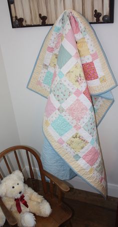 a teddy bear sitting on a chair next to a quilt