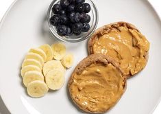 a white plate topped with two pieces of bread next to sliced bananas and blueberries