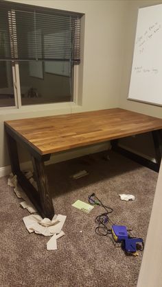 a wooden table sitting on top of a carpeted floor next to a whiteboard