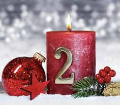 a red candle sitting next to a christmas ornament on top of snow covered ground