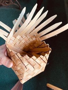 a person holding a basket made out of wood sticks and paper with scissors in the background