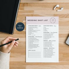 a person holding a pen and writing on a wedding shot list next to a laptop