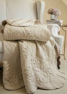 a white chair with a blanket on top of it next to a table and flowers