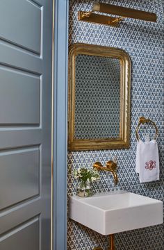 a bathroom with blue and white wallpaper, gold framed mirror, sink and towel rack