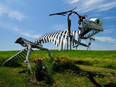 a large metal skeleton sitting on top of a lush green field next to tall grass