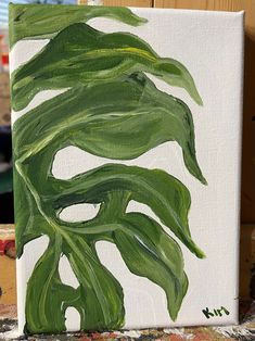 a painting of a green leaf on a white canvas with paintbrushes in the background