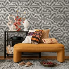 an orange bench in front of a wall with geometric designs on it and two vases filled with flowers