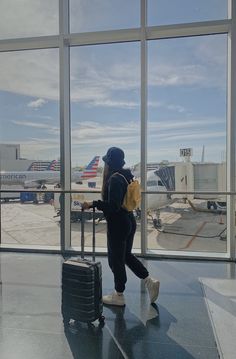 a woman is walking through an airport with her luggage and looking out the window at planes