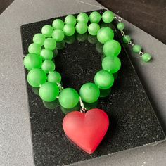 Destaca con este impresionante y único collar llamativo verde impreso en 3D. Diseñado con cuentas gruesas e inspirado en el icónico estilo Iris Apfel, este collar irradia elegancia, confianza e individualidad. El vibrante color verde añade un toque de frescura a cualquier conjunto, convirtiéndolo en un accesorio versátil y llamativo. La pieza central de este collar presenta un impresionante colgante de corazón rojo, que simboliza el amor y la pasión. Elaborado con tecnología avanzada de impresió Green Heart-shaped Beaded Necklace Gift, Green Pendant Necklace For Valentine's Day, Bold Resin Jewelry For Gifts, Bold Resin Jewelry For Gift, Valentine's Day Green Necklace With Heart Charm, Green Jewelry With Heart Charm And Round Beads, Green Heart-shaped Jewelry For Party, Green Heart Necklace For Gift, Handmade Bold Resin Jewelry