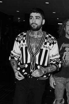 two men with tattoos and piercings are walking through an airport terminal, one is wearing a striped jacket