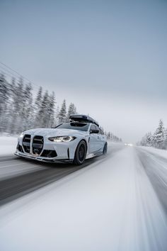 a white car driving down a snow covered road with trees in the backgroud