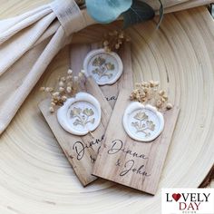 two wooden tags with flowers on them are sitting on a wood plate next to a flower bouquet