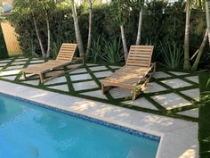 two lawn chairs next to a swimming pool with grass on the ground and palm trees in the background