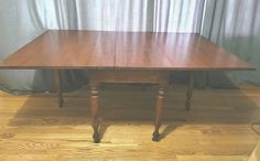 a wooden table sitting on top of a hard wood floor next to a curtained window