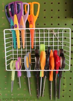 there are many different colored scissors hanging on the pegs in this wall rack,