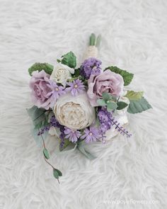 a bridal bouquet with purple flowers and greenery on a white furnishing