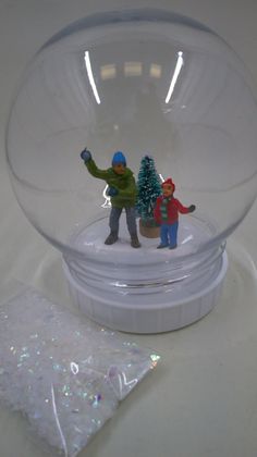 two small figurines in a glass bowl on a white table top with snow flakes