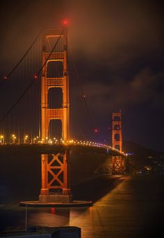 the golden gate bridge lit up at night with lights shining on it's sides