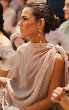 a woman sitting in front of a group of people wearing large gold earring's