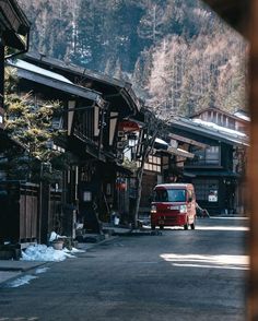 a red bus driving down a street next to tall wooden buildings with snow on the ground